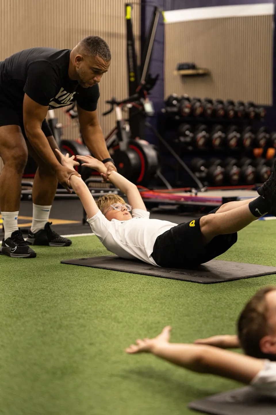 Coach guiding a young athlete through a floor movement in the Playermade gym