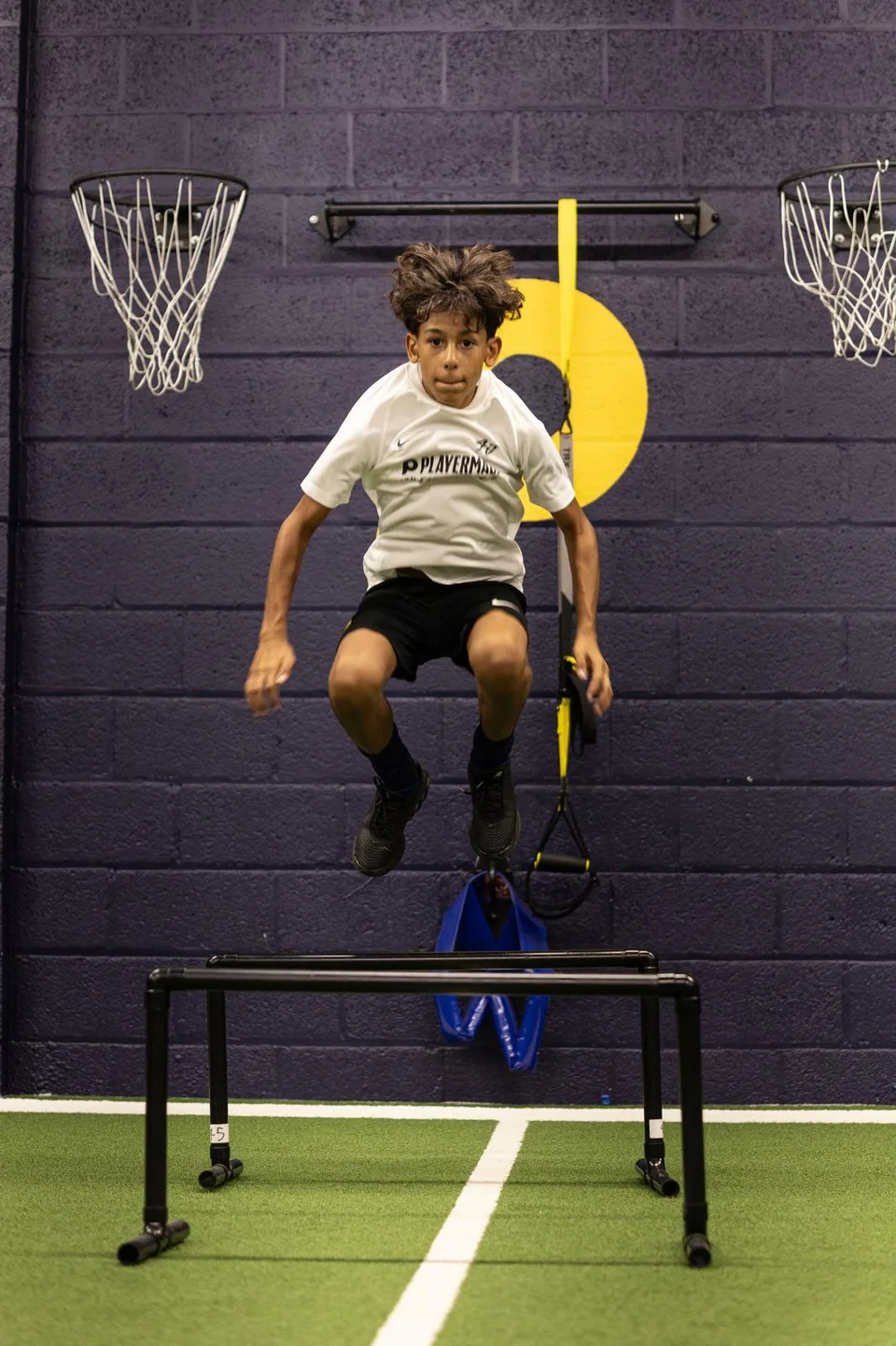 Young athlete jumping over a hurdle in the Playermade gym