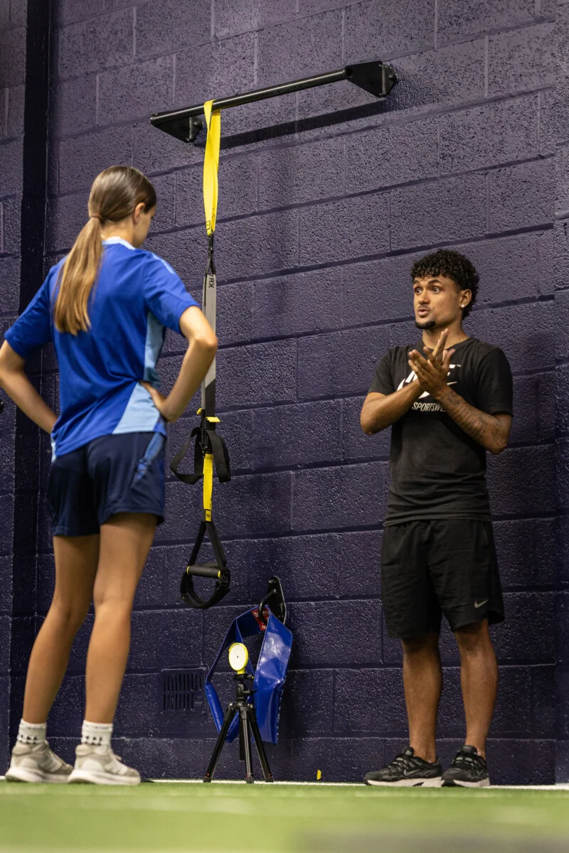 A coach explaining an exercise to a junior athlete beside suspension-training straps