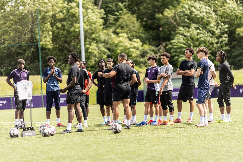 A group of footballers listening to their Playermade coach on the pitch