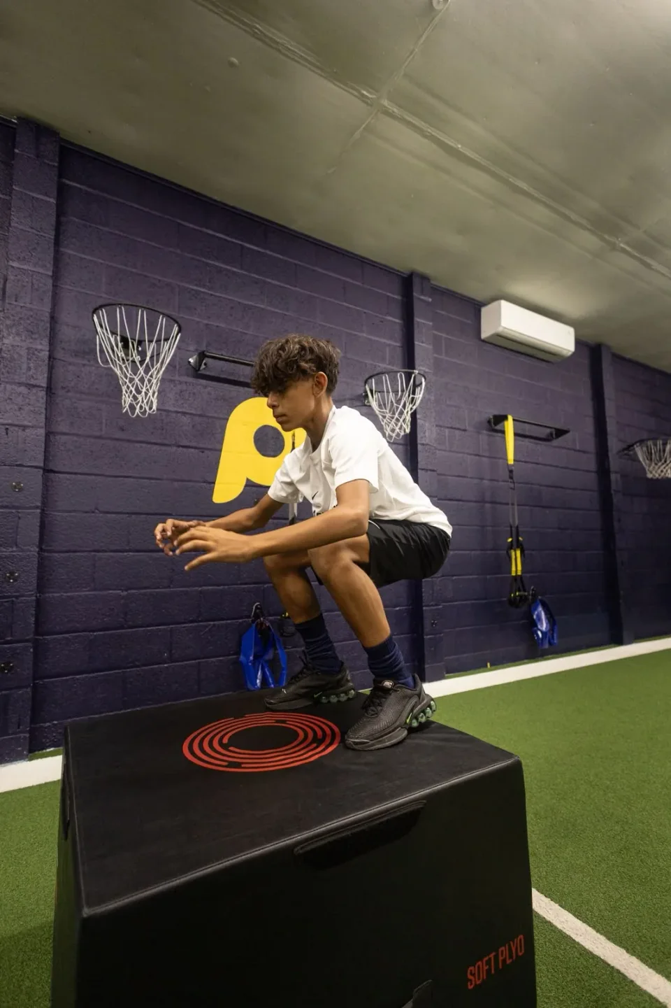 A junior athlete landing a box jump in the Playermade gym