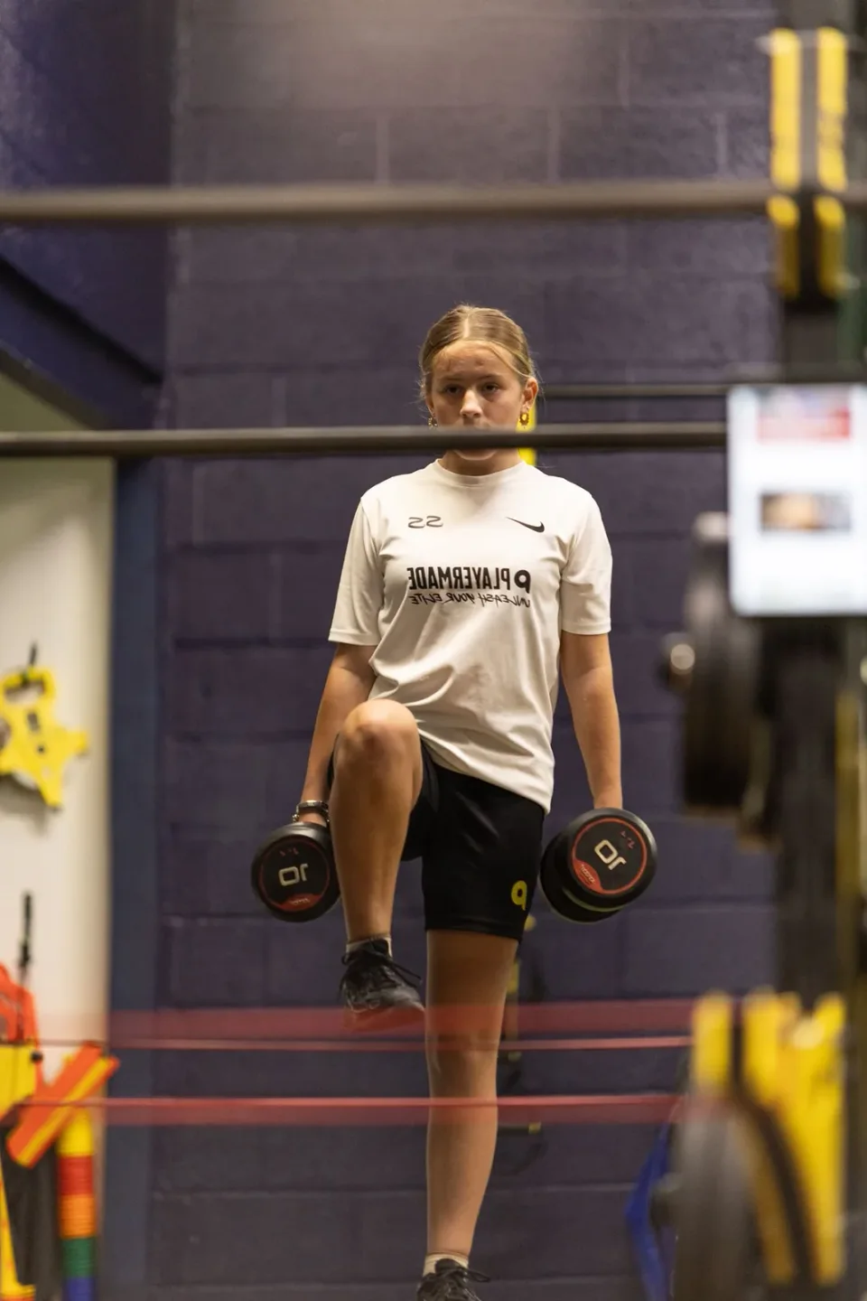 A junior athlete raising one knee while holding dumbbells in the gym