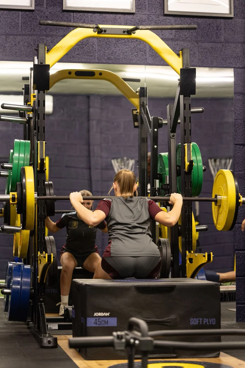 An athlete performing a barbell box squat at Playermade