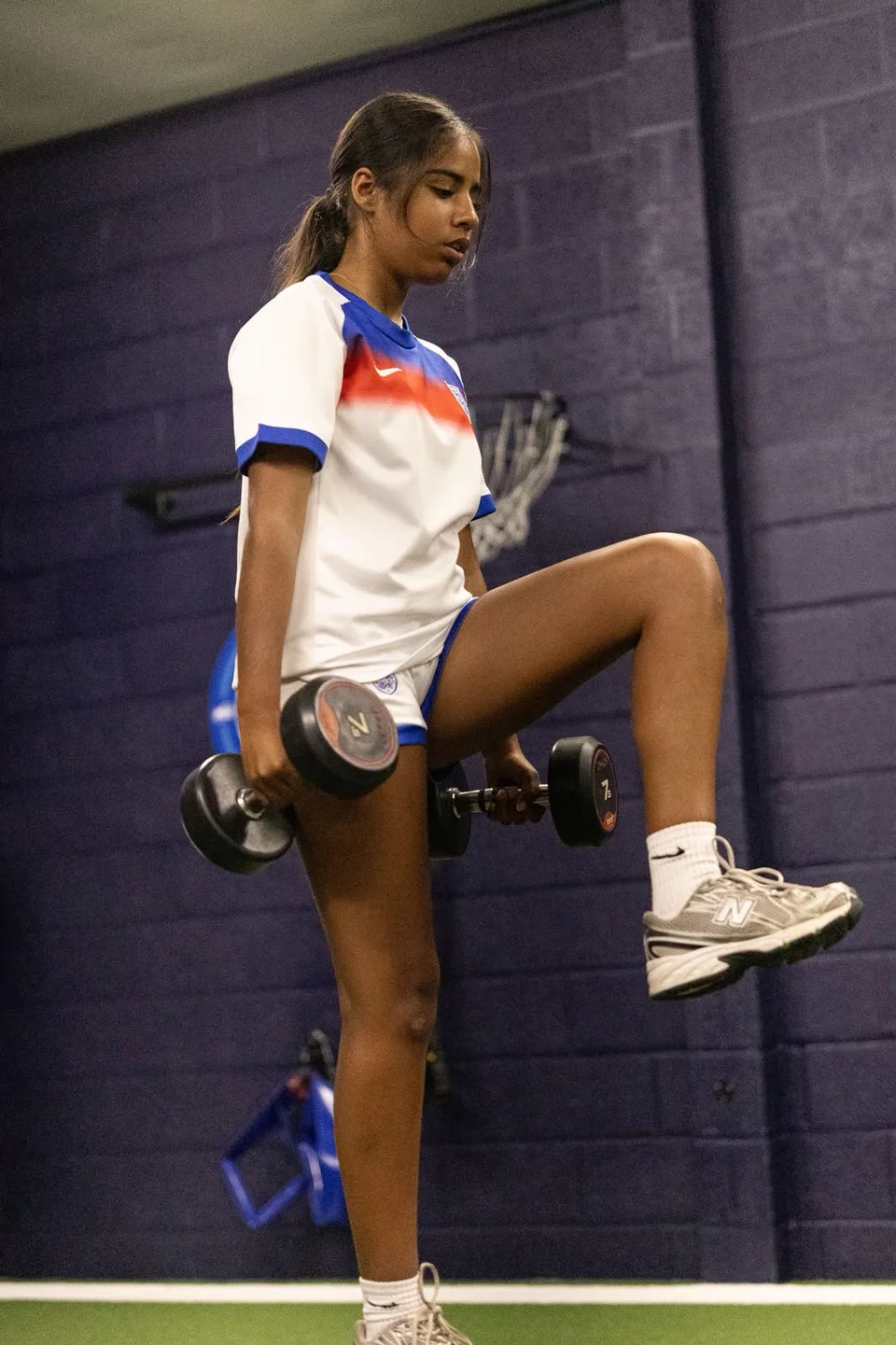 An athlete raising one knee while holding dumbbells