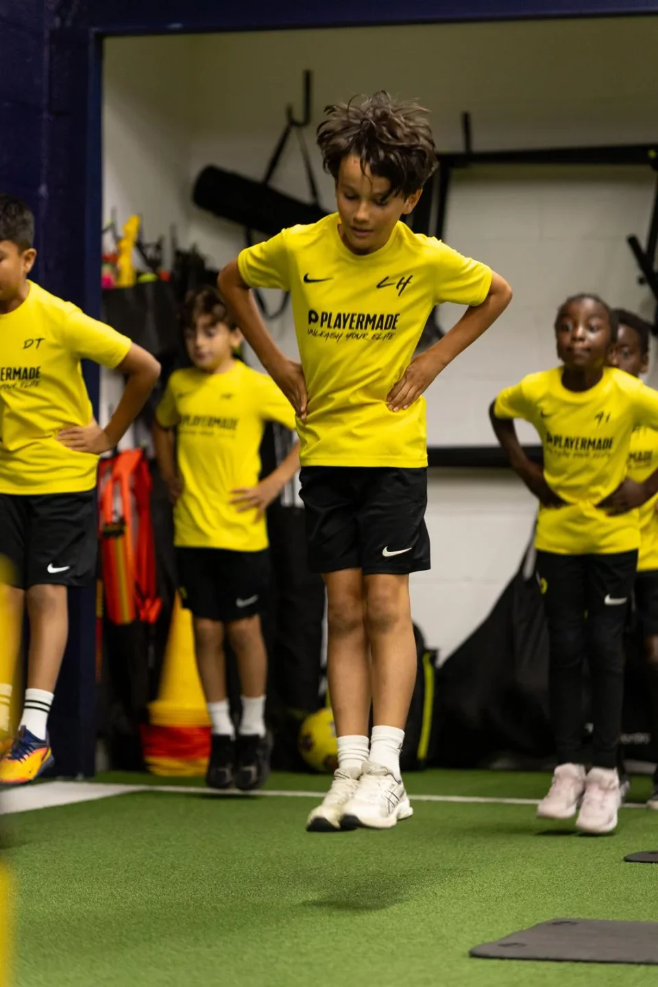 Junior athletes practising jumps together on the indoor turf in Playermade training kit