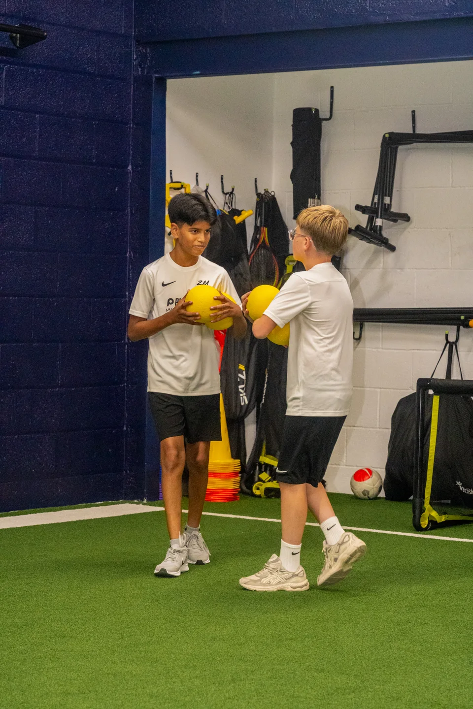 Two junior athletes training together with medicine balls on the indoor turf