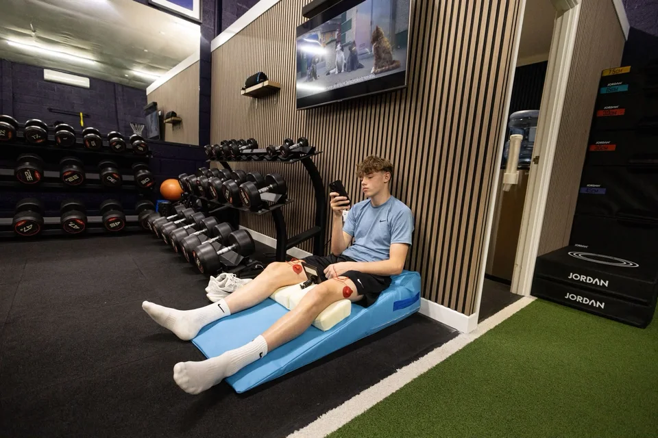 An athlete seated on a mat during a recovery session with electrode pads on his legs