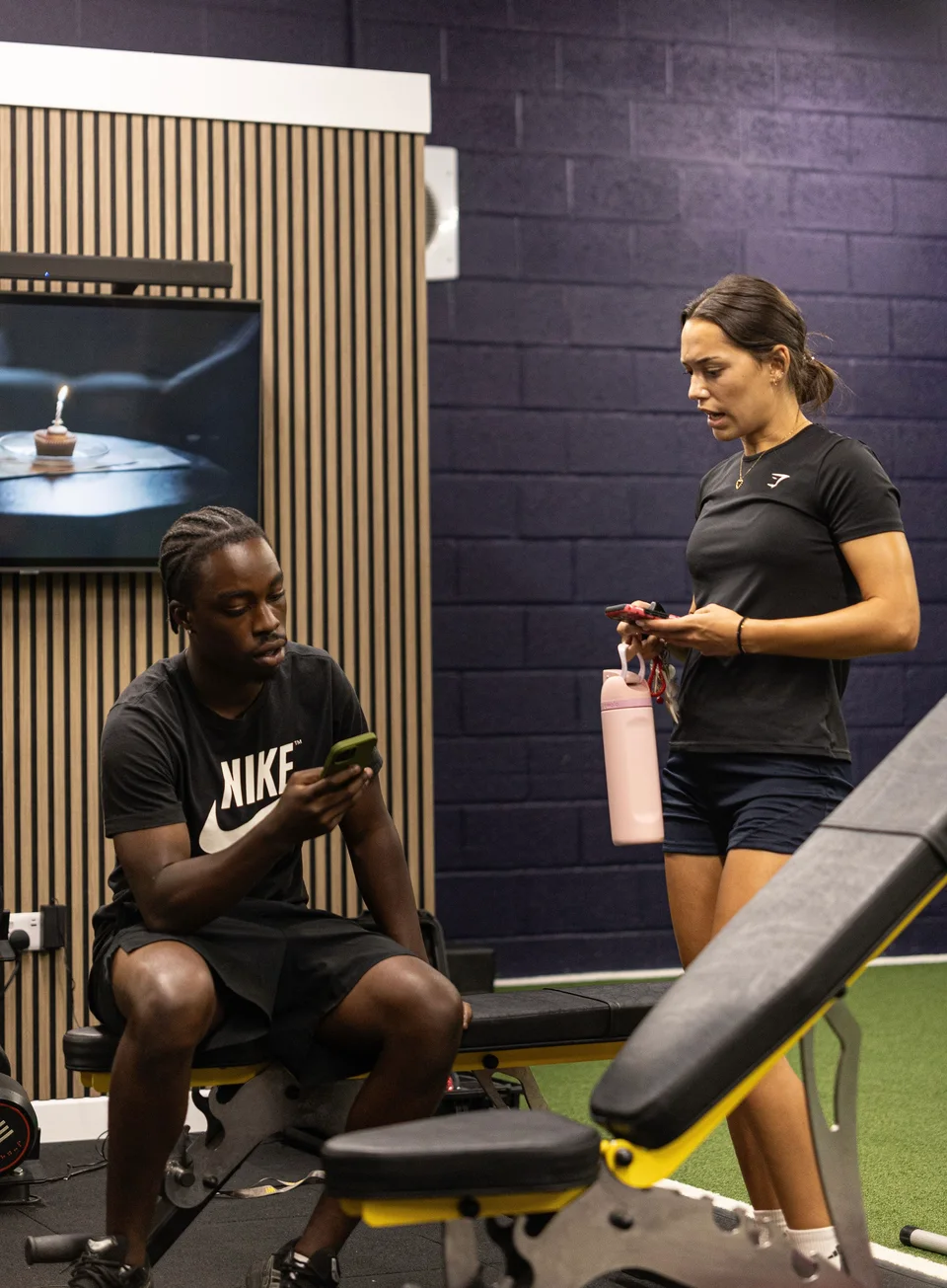 A coach and athlete reviewing their online training in the gym