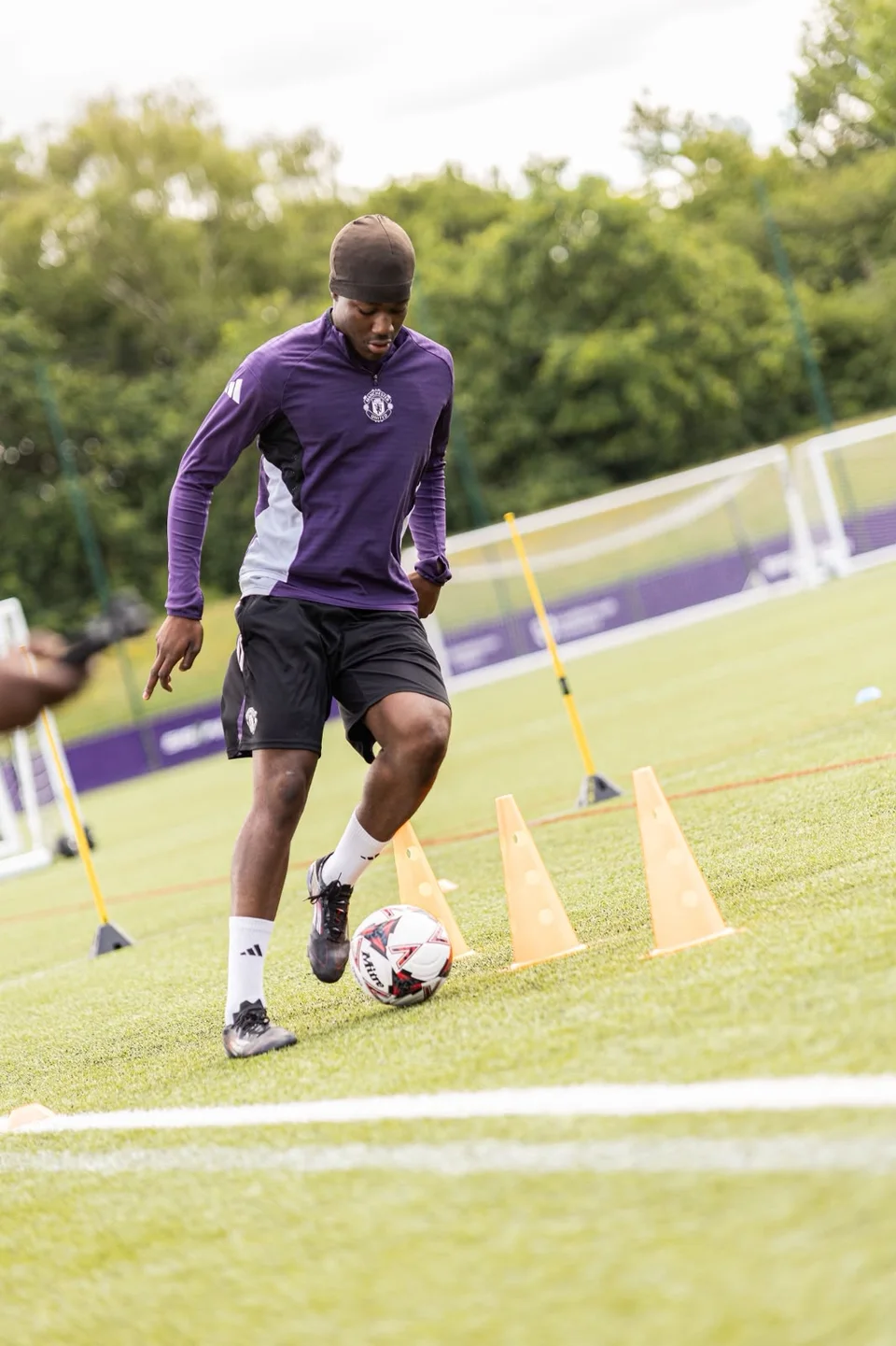 A footballer controlling a ball between training cones