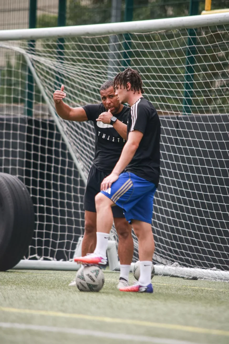 A Playermade coach explaining technique to a footballer beside a goal