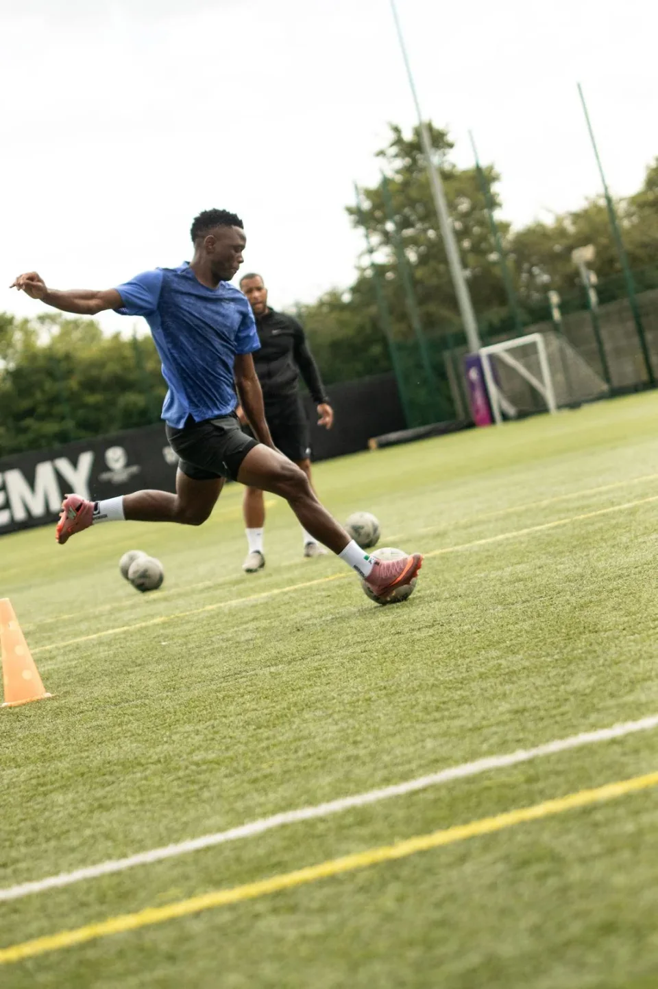 A footballer practising ball striking with a coach on the pitch