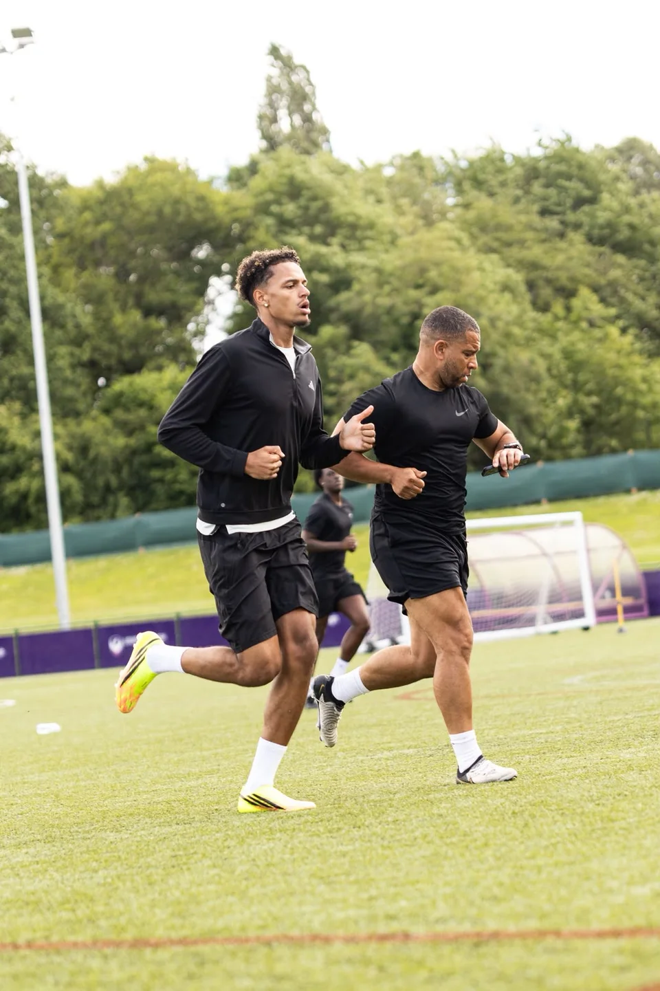 Athletes warming up alongside a coach on the training pitch