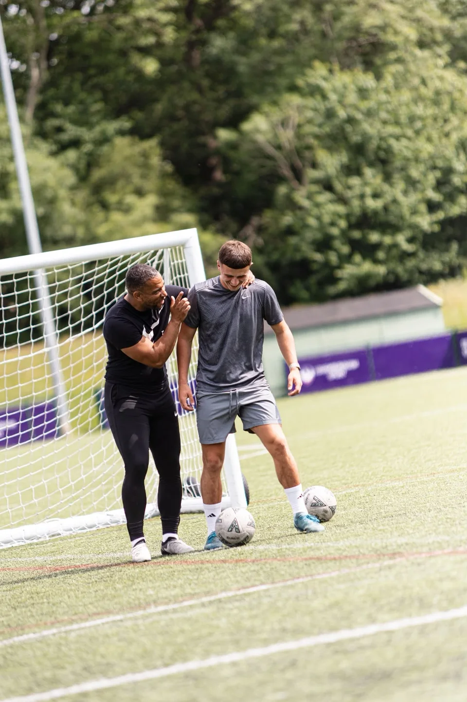 A Playermade coach and a footballer sharing feedback beside a goal