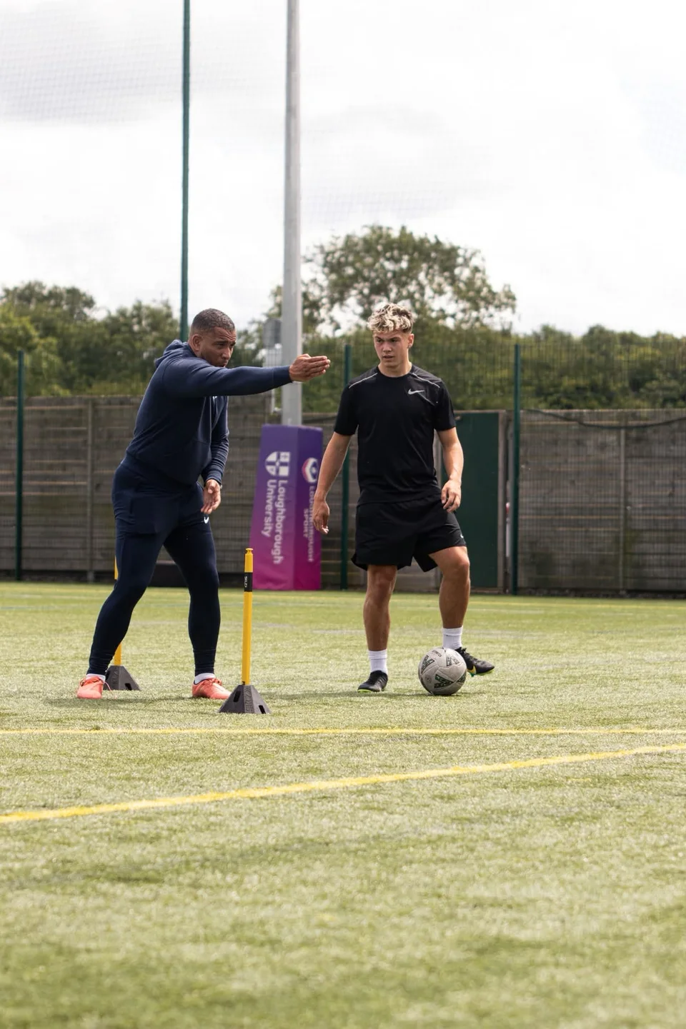 A coach explaining positioning to a footballer beside a training pole