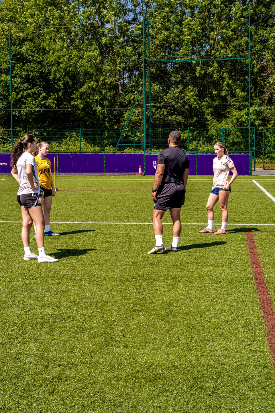 Female footballers discussing a drill with their coach on the pitch