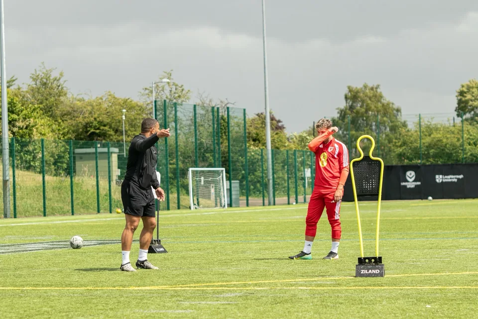 A coach and a footballer working beside a training mannequin