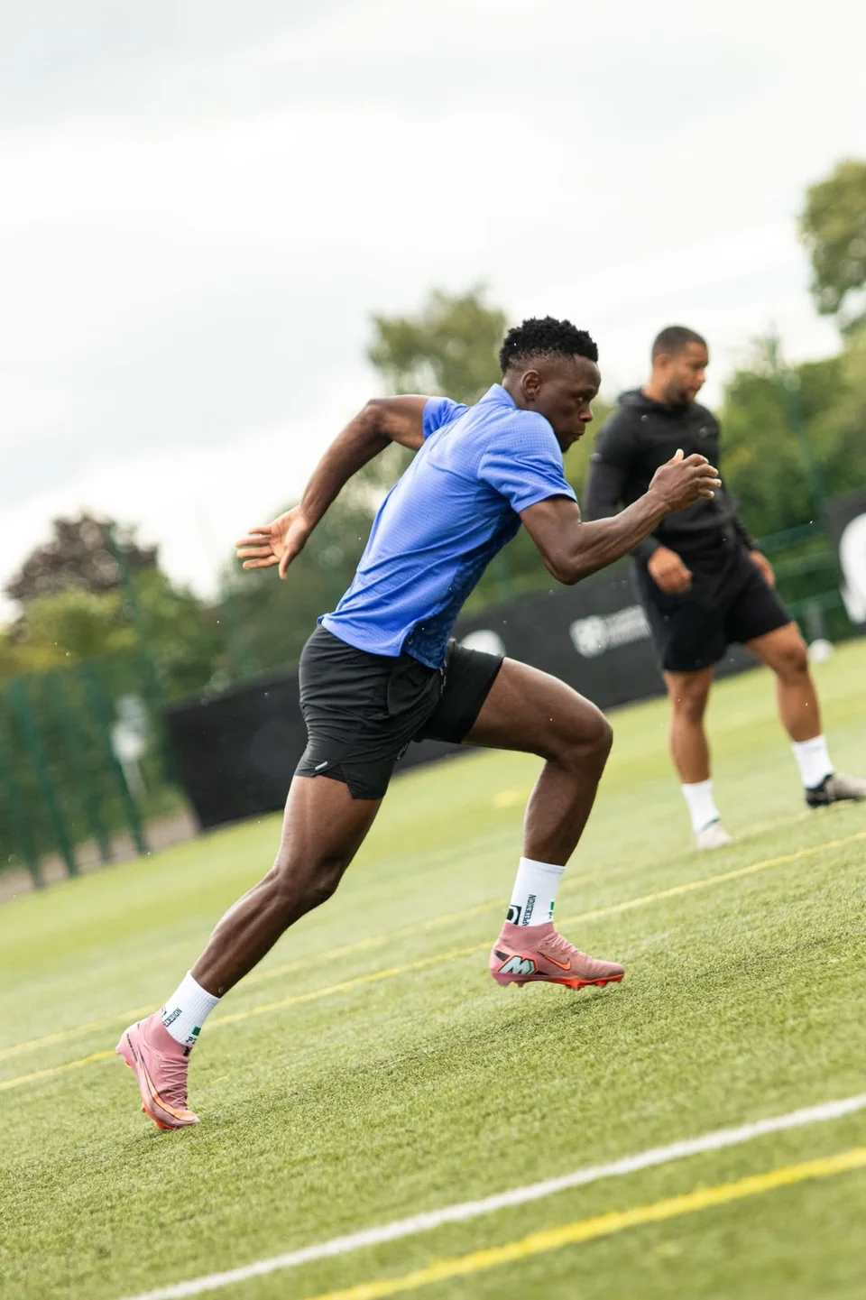 A footballer accelerating past a coach on the training pitch