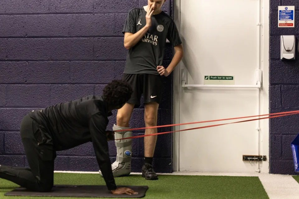 A coach supporting a junior athlete wearing a walking boot during rehabilitation