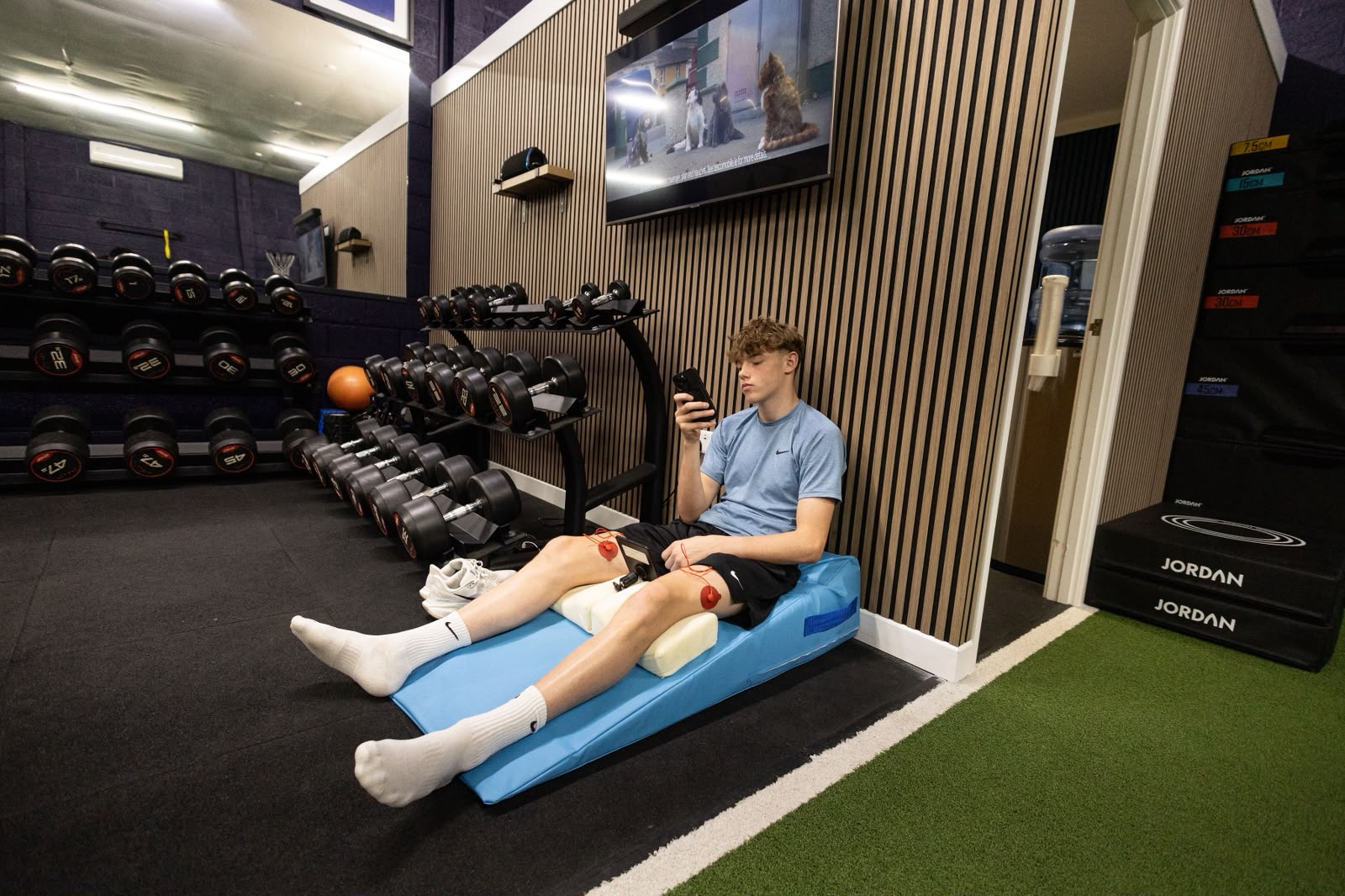 An athlete seated on a mat during a recovery session with electrode pads on his legs